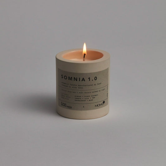 Vela aromática Somnia 1.0 de Momo Cotton con llama encendida sobre fondo gris