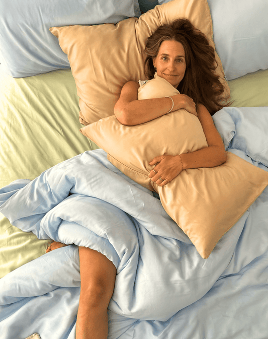 Mujer en cama sosteniendo juego de sábanas de algodón melocotón con edredón azul, sábana verde claro visible debajo