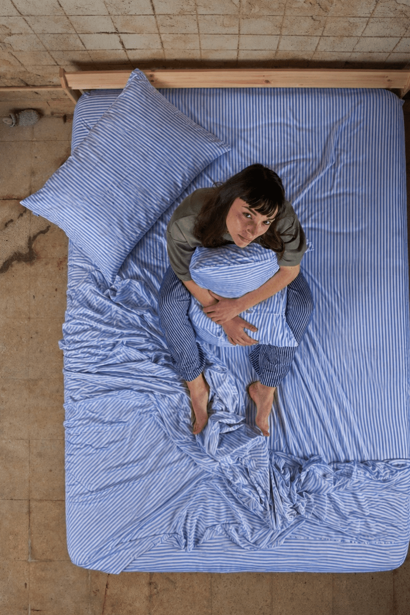 Mujer acostada en la cama con juego de sábanas de algodón bambú a rayas azules, vista superior