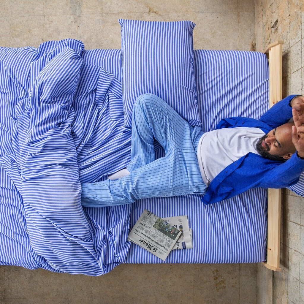 Hombre acostado en funda de edredón con patrón azul y blanco en la cama con periódico, vista superior