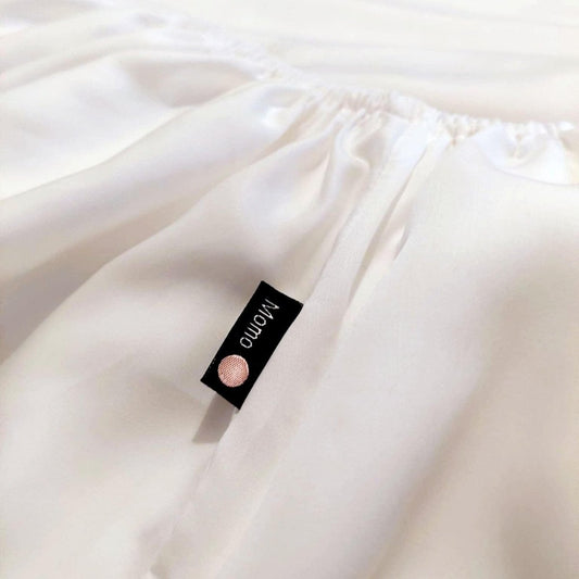 Sábana bajera blanca de bambú con etiqueta de marca momo-cotton en la superficie del tejido doblado