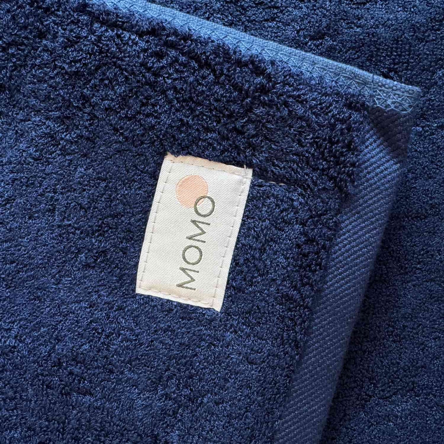 Tapete de baño azul marino Wabi-sabi de Momo Cotton con etiqueta de marca visible en tela texturizada