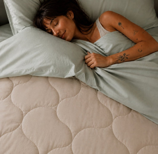 Mujer durmiendo plácidamente en cama con edredón acolchado beige y sábanas gris claro de Momo Cotton