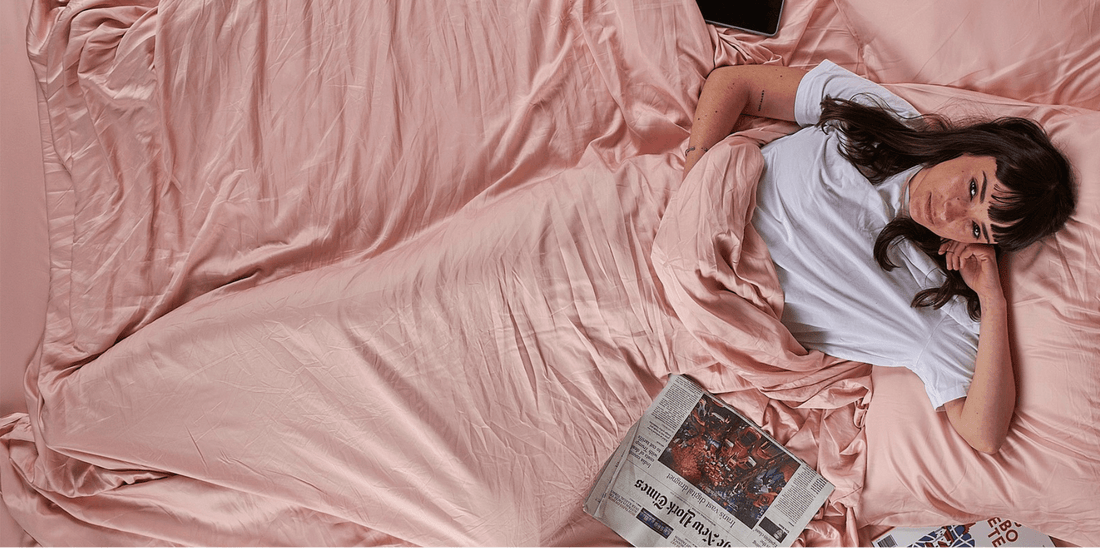 Mujer tumbada en cama con ropa de cama rosa leyendo periódico, decoración de dormitorio primaveral.