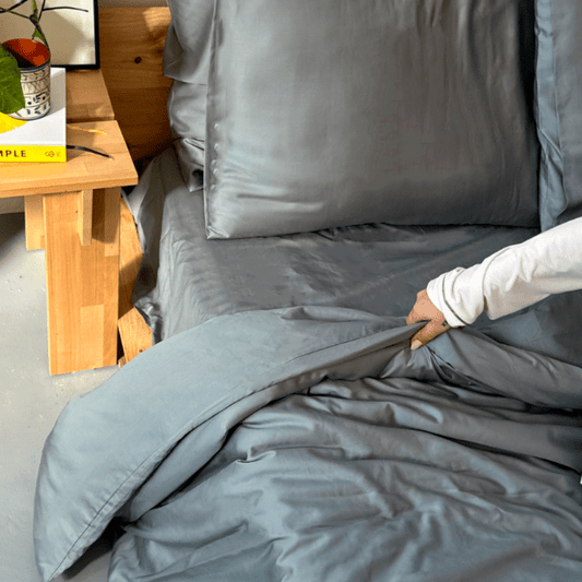Mujer tocando ropa de cama de bambú gris en cama con mesa de madera al fondo