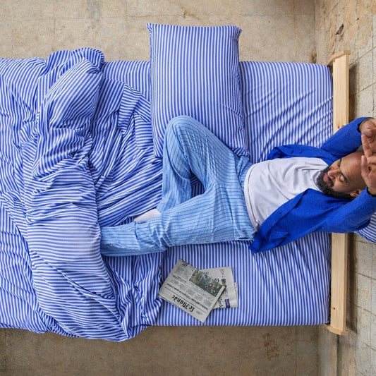 Hombre durmiendo cómodamente en sábanas de bambú azules y blancas a rayas.