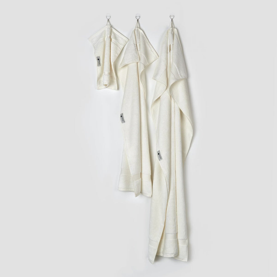 Three cream bamboo towels hanging on hooks displaying face, hand, and bath sizes from the Alba collection by momo-cotton