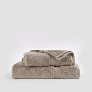 Juego de toallas de bambú beige apiladas, mostrando paño facial, toalla de mano y toalla de baño sobre fondo blanco