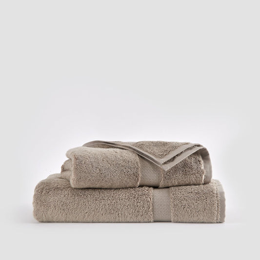 Juego de toallas de bambú beige apiladas, mostrando paño facial, toalla de mano y toalla de baño sobre fondo blanco