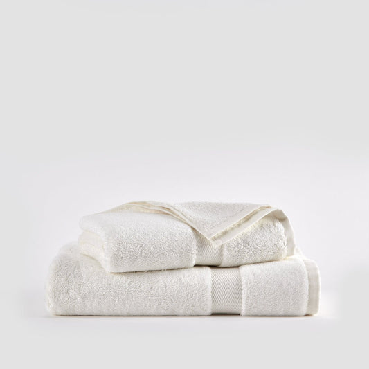 Tres toallas de bambú color crema apiladas sobre fondo blanco - juego de toalla facial, de mano y de baño