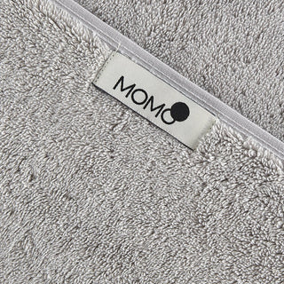 Toalla de bambú gris con etiqueta de marca momo-cotton en ribete blanco, detalle de textura suave
