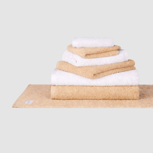 Juego de toallas de algodón apiladas en beige y blanco de Momo Cotton sobre fondo neutro