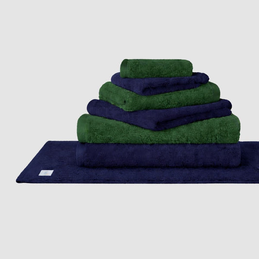 Juego de toallas Wabi Sabi apiladas en azul marino y verde de Momo Cotton sobre fondo neutro