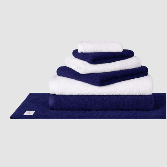 Juego de toallas Wabi Sabi azul marino y blanco apiladas en tapete de baño azul marino sobre fondo neutro