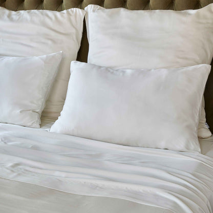 White top sheet on bed with pillows and beige padded headboard