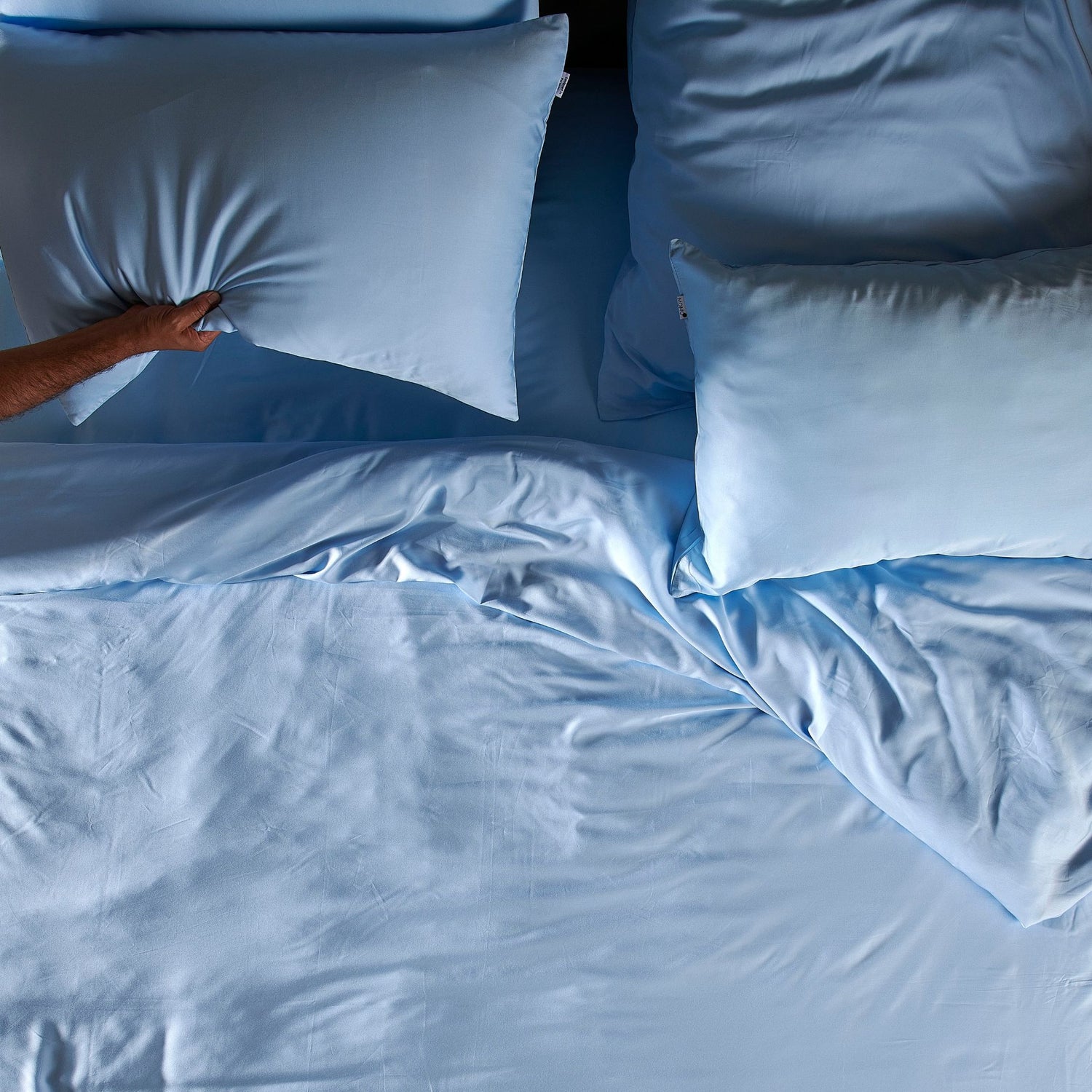 Persona colocando juego de sábanas de bambú azul claro con almohadas en la cama, mostrando textura y suavidad