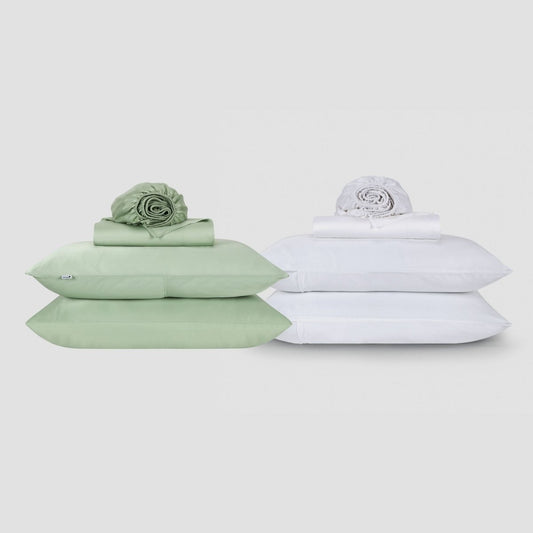 Dos juegos de sábanas Momo de algodón uno al lado del otro, uno verde salvia y otro blanco, cada uno apilado con ropa de cama doblada