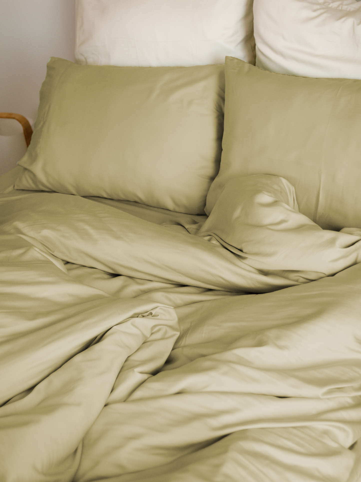 Cama com capa de edredão bege areia, almofadas bege e almofadas brancas atrás – macio e sustentável