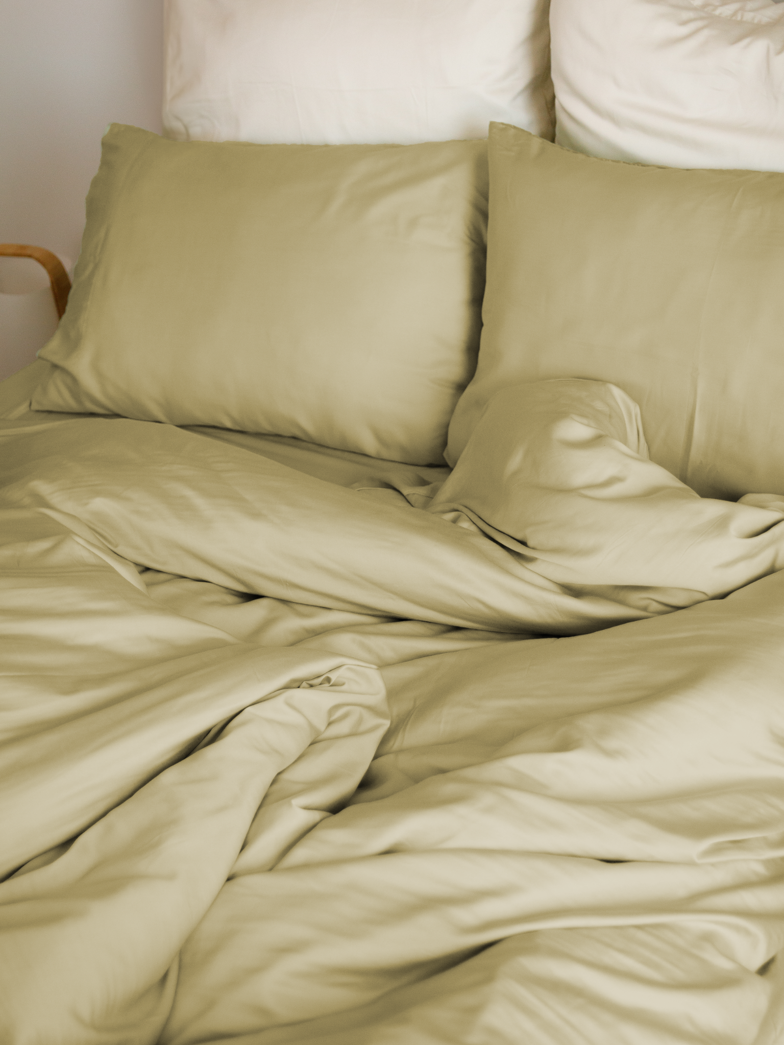 Cama com capa de edredão bege areia, almofadas bege e almofadas brancas atrás – macio e sustentável