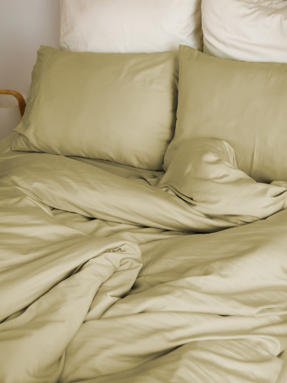 Cama com capa de edredão bege areia, almofadas bege e almofadas brancas atrás – macio e sustentável