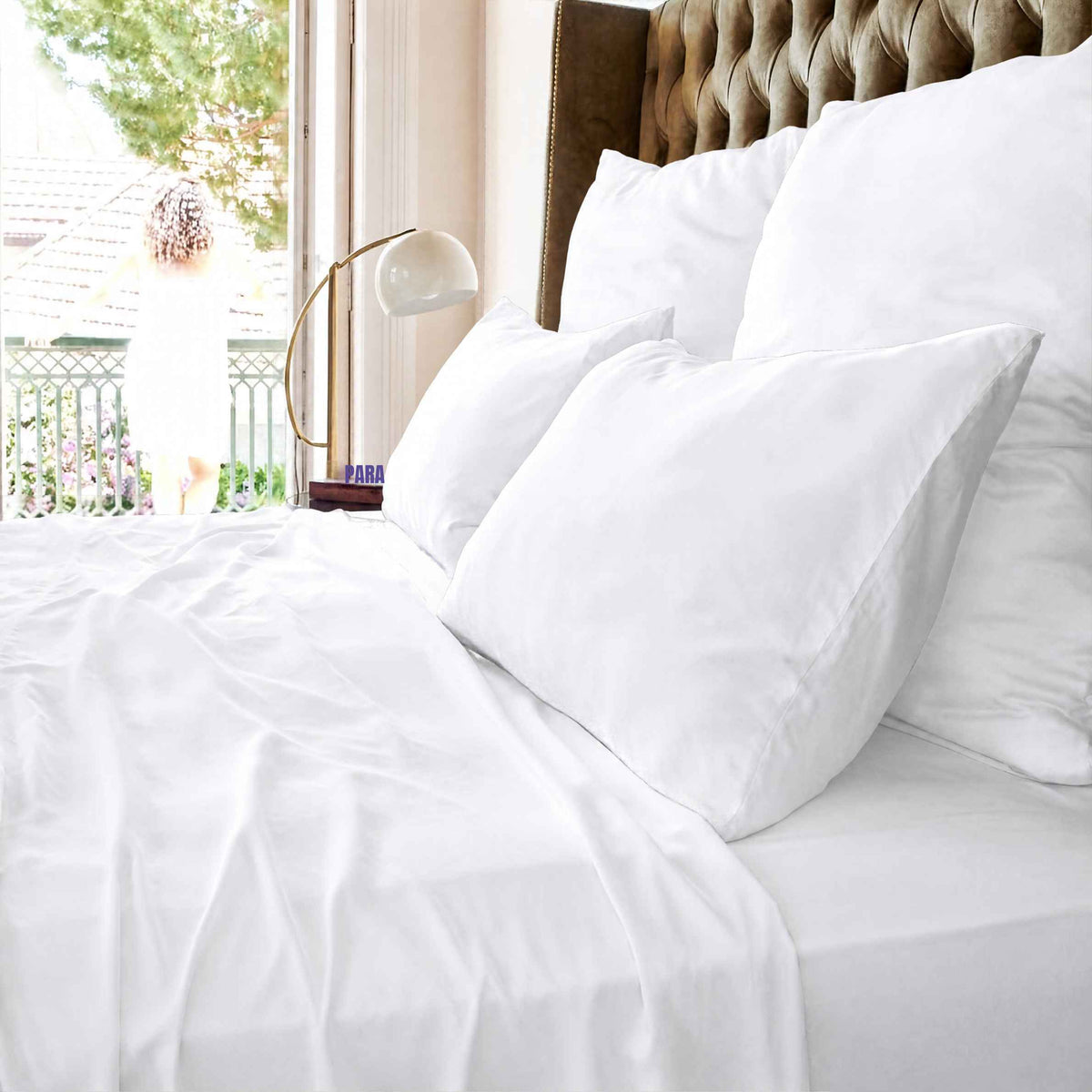 White top sheet on bed with pillows and upholstered headboard by window overlooking balcony