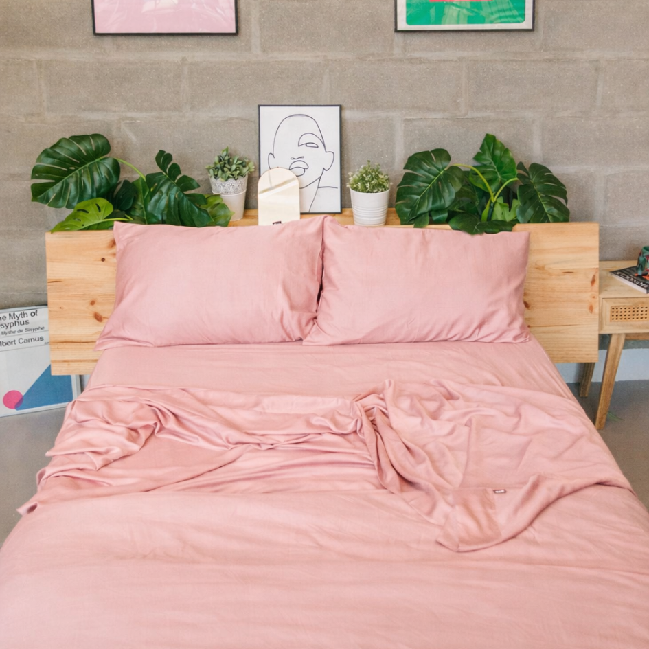 Pink bamboo bed linen set styled in a minimalist bedroom with a green headboard and neutral cushions.