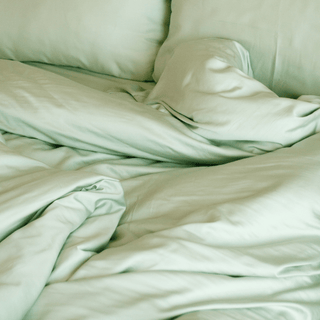 Juego de cama de bambú verde salvia exhibido en la cama mostrando sábana ajustable, sábana plana, funda de almohada y funda nórdica